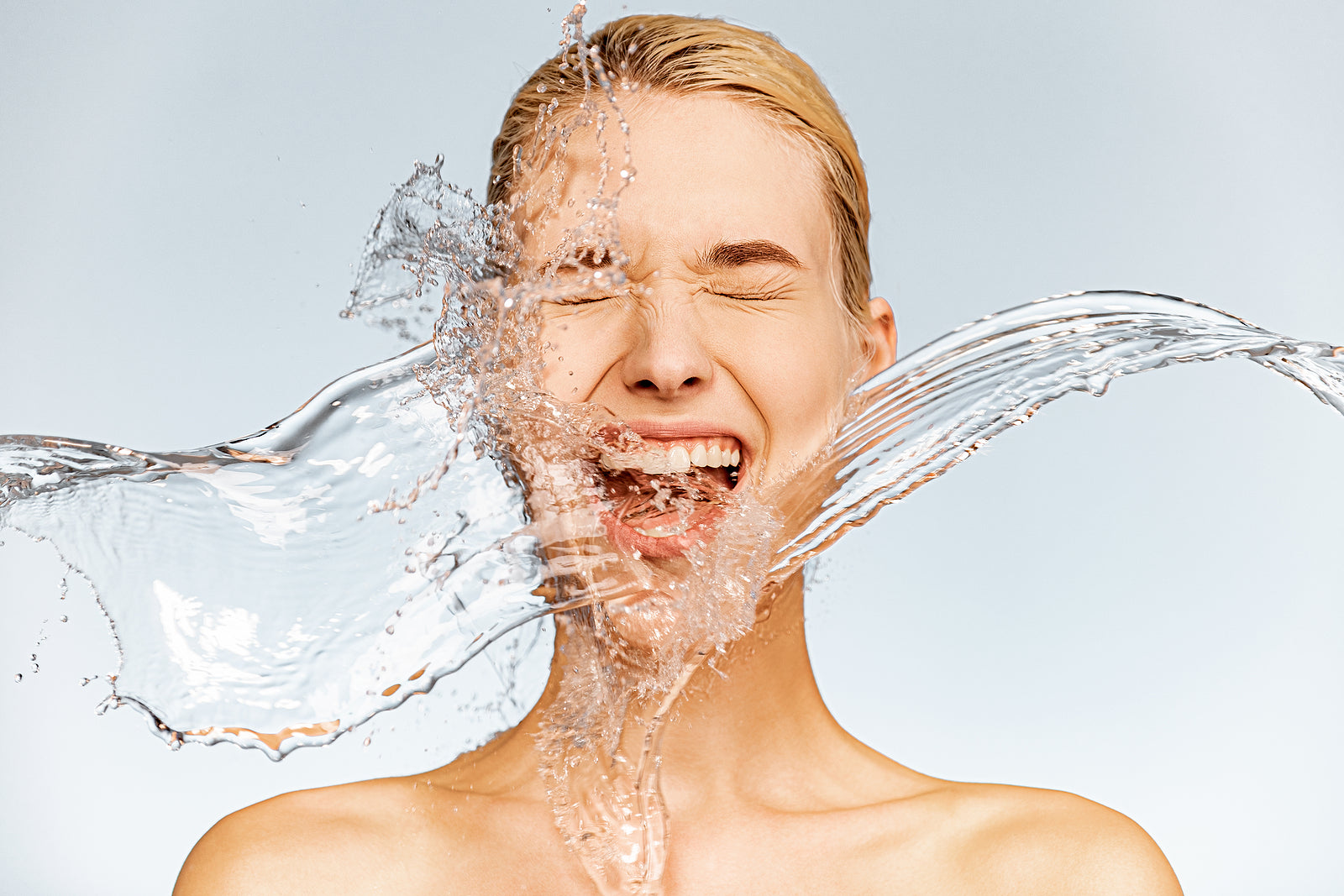 Woman being splashed in the face with water - a representation of the hydrating benefits of hyaluronic acid