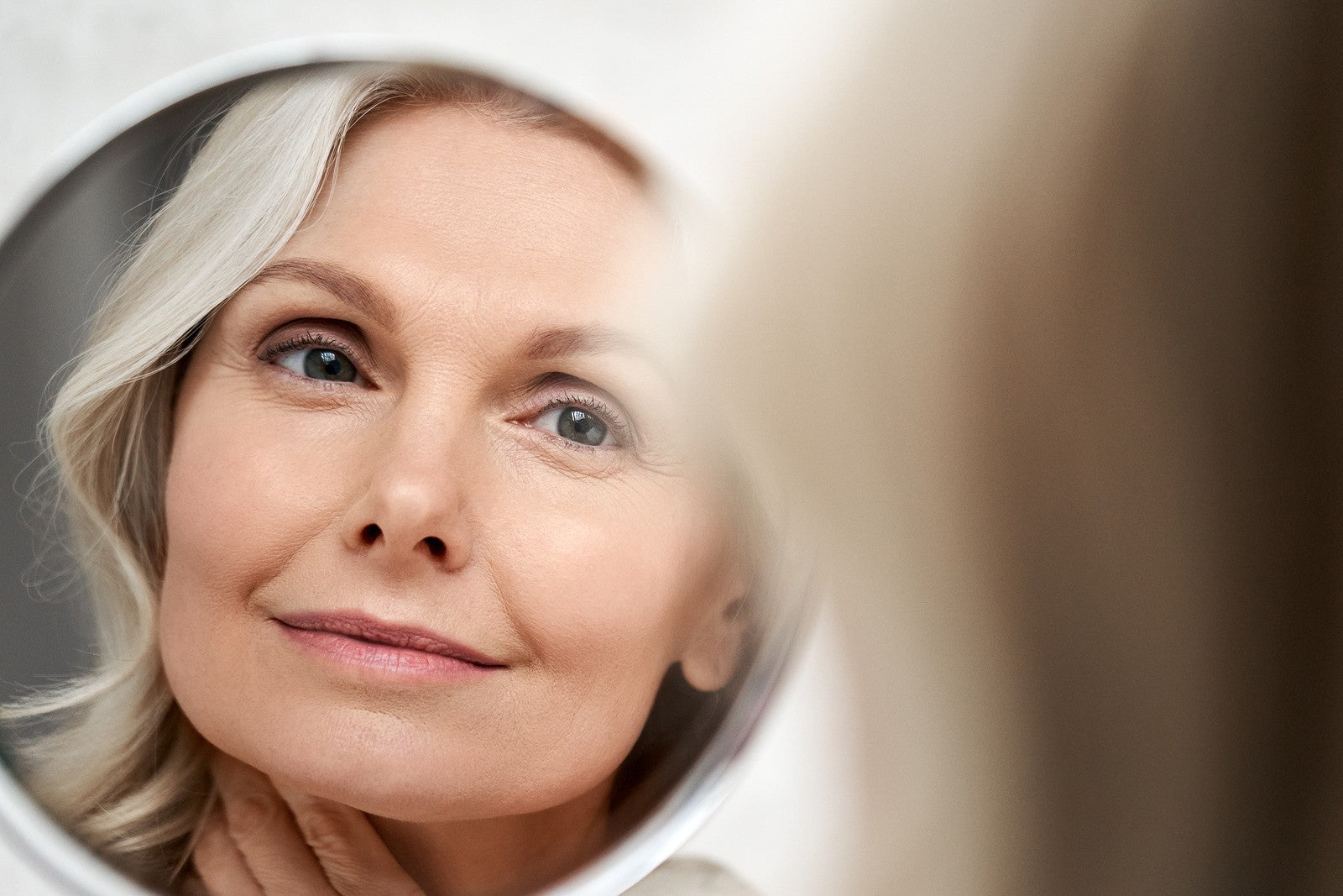 Older woman looking at her skin in the mirror - how to combat signs of aging